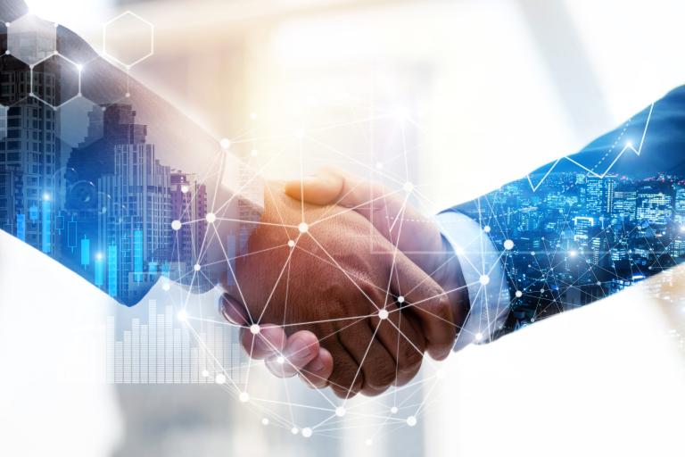 A close‑up of two people shaking hands, with a digital network graphic and a cityscape blended into the background to represent technology and partnership.