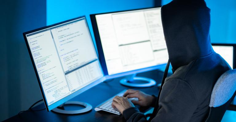 Man in hoodie views dual monitor computer screens
